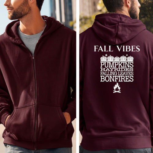 Maroon Gildan hoodie featuring a white “FALL VIBES” design on the back with stacked seasonal words: “PUMPKINS, HAYRIDES, FALLING LEAVES, BONFIRES,” framed by pumpkins above and a bonfire icon below. A cozy, festive graphic perfect for autumn lovers and fall adventures.