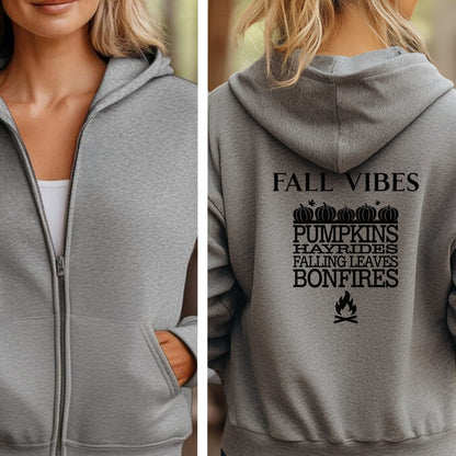 Sport Grey Gildan hoodie featuring a black “FALL VIBES” design on the back with stacked seasonal words: “PUMPKINS, HAYRIDES, FALLING LEAVES, BONFIRES,” framed by pumpkins above and a bonfire icon below. A cozy, festive graphic perfect for autumn lovers and fall adventures.