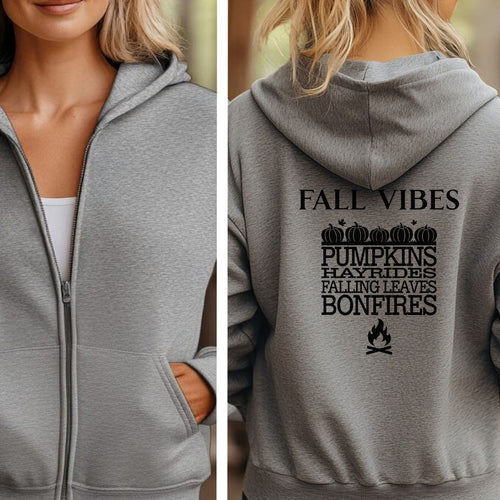 Sport Grey Gildan hoodie featuring a black “FALL VIBES” design on the back with stacked seasonal words: “PUMPKINS, HAYRIDES, FALLING LEAVES, BONFIRES,” framed by pumpkins above and a bonfire icon below. A cozy, festive graphic perfect for autumn lovers and fall adventures.