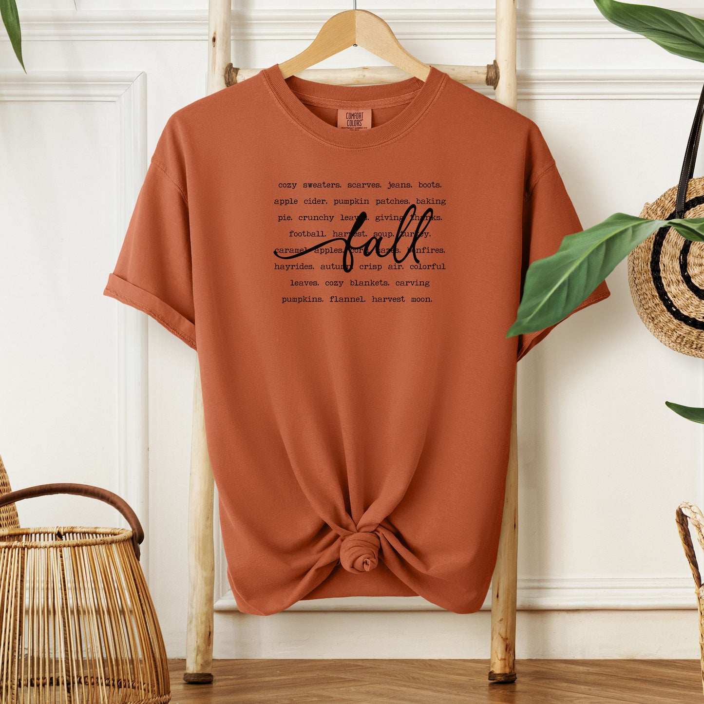 Yam T-shirt with a cozy fall-themed text design featuring words like cozy sweaters, pumpkin patches, apple cider, hayrides, football, bonfires, flannel, and harvest moon. The word “Fall” stands out in a large handwritten script across the center, celebrating autumn vibes and seasonal favorites. Perfect for fall lovers and casual outfits.