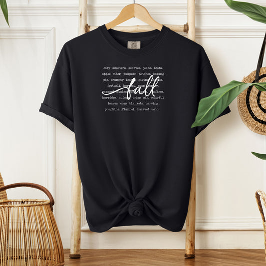 Black T-shirt with a cozy fall-themed text design featuring words like cozy sweaters, pumpkin patches, apple cider, hayrides, football, bonfires, flannel, and harvest moon. The word “Fall” stands out in a large handwritten script across the center, celebrating autumn vibes and seasonal favorites. Perfect for fall lovers and casual outfits.