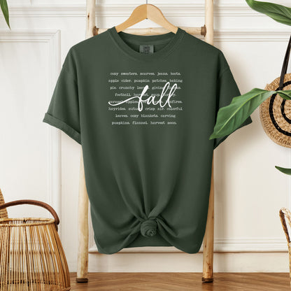 Hemp color T-shirt with a cozy fall-themed text design featuring words like cozy sweaters, pumpkin patches, apple cider, hayrides, football, bonfires, flannel, and harvest moon. The word “Fall” stands out in a large handwritten script across the center, celebrating autumn vibes and seasonal favorites. Perfect for fall lovers and casual outfits.