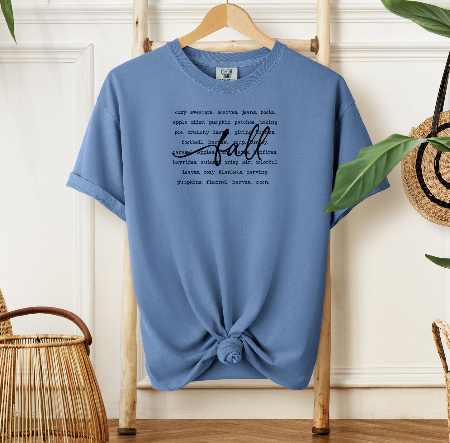 Washed Denim T-shirt with a cozy fall-themed text design featuring words like cozy sweaters, pumpkin patches, apple cider, hayrides, football, bonfires, flannel, and harvest moon. The word “Fall” stands out in a large handwritten script across the center, celebrating autumn vibes and seasonal favorites. Perfect for fall lovers and casual outfits.