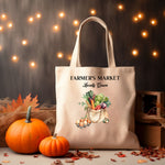 A Natural Tote bag with 'Farmer's Market Locally Grown' text and vegetable in a tote bag illustration with carton of eggs next to it sitting on a table with pumpkins and autumn decor around it.