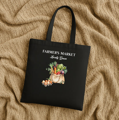 Black tote bag with 'Farmer's Market Locally Grown' text and vegetable illustration on a beige fabric background