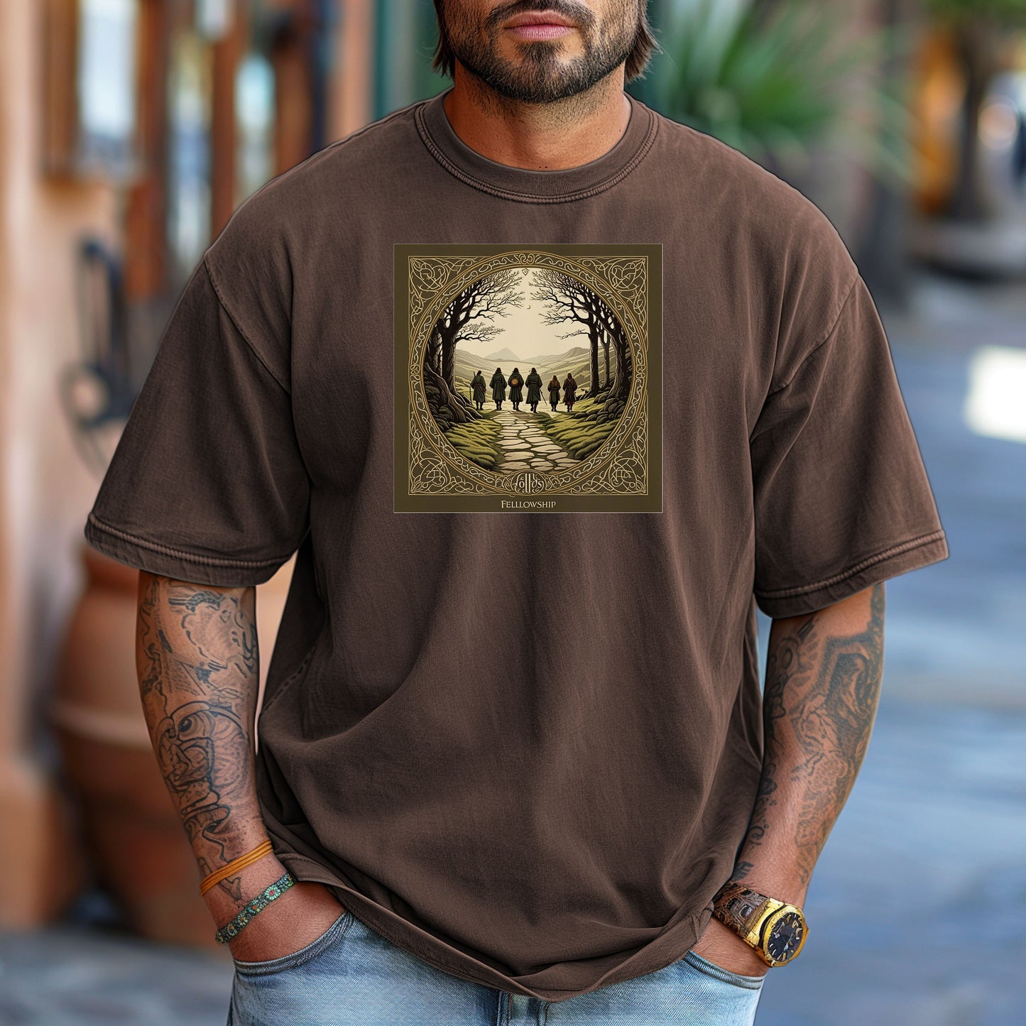 Espresso “Fellowship” T-shirt featuring a fantasy-inspired design of five cloaked figures walking along a stone path toward distant mountains. The scene is framed by intricate Celtic-style borders with bare trees arching overhead, creating an adventurous and mythical atmosphere. Perfect for fans of epic journeys, fantasy worlds, and storytelling-inspired apparel.