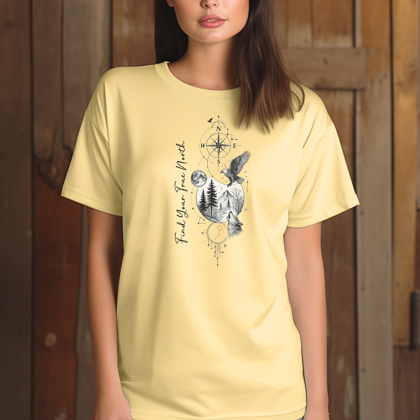 Person wearing a banana T-shirt featuring a “Find Your True North” design with a vertical compass, full moon, pine trees, mountains, soaring eagle, and howling wolf in detailed black and white sketch style. The design blends celestial and wilderness elements, symbolizing adventure, guidance, and a connection to nature. Perfect for outdoor lovers, travelers, and free spirits seeking inspiration and direction.