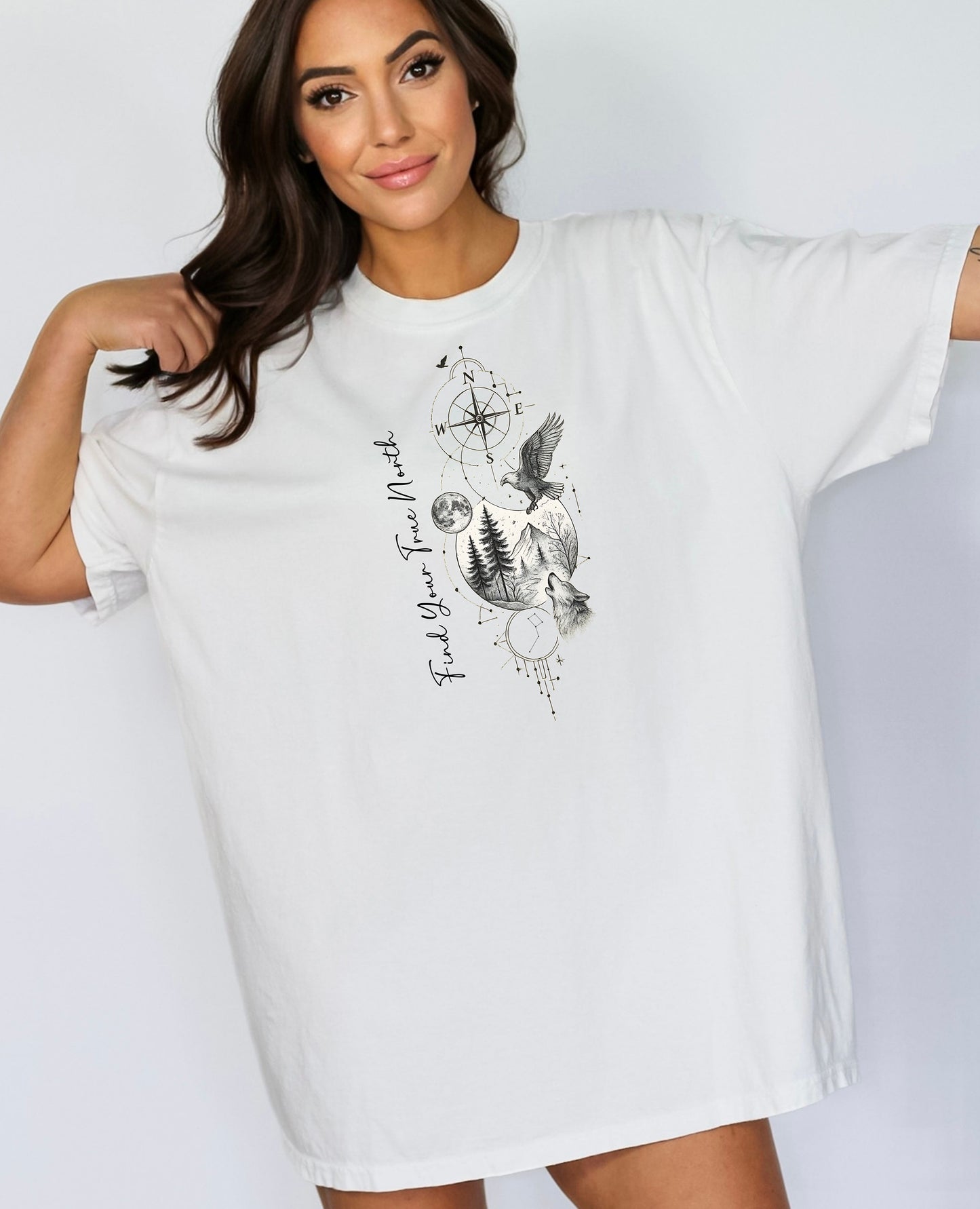 Person wearing a classic white T-shirt featuring a “Find Your True North” design with a vertical compass, full moon, pine trees, mountains, soaring eagle, and howling wolf in detailed black and white sketch style. The design blends celestial and wilderness elements, symbolizing adventure, guidance, and a connection to nature. Perfect for outdoor lovers, travelers, and free spirits seeking inspiration and direction.