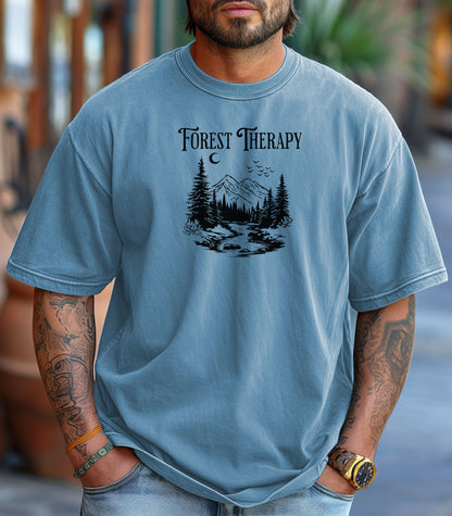 Person wearing a Washed Denim t-shirt featuring a black “Forest Therapy” design with a peaceful mountain scene, pine trees, a flowing river, birds, and a crescent moon. The perfect tee for nature lovers, hikers, and outdoor enthusiasts seeking serenity and scenic vibes.