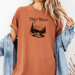 Person wearing a yam t-shirt featuring a black “Forest Therapy” design with a peaceful mountain scene, pine trees, a flowing river, birds, and a crescent moon. The perfect tee for nature lovers, hikers, and outdoor enthusiasts seeking serenity and scenic vibes.
