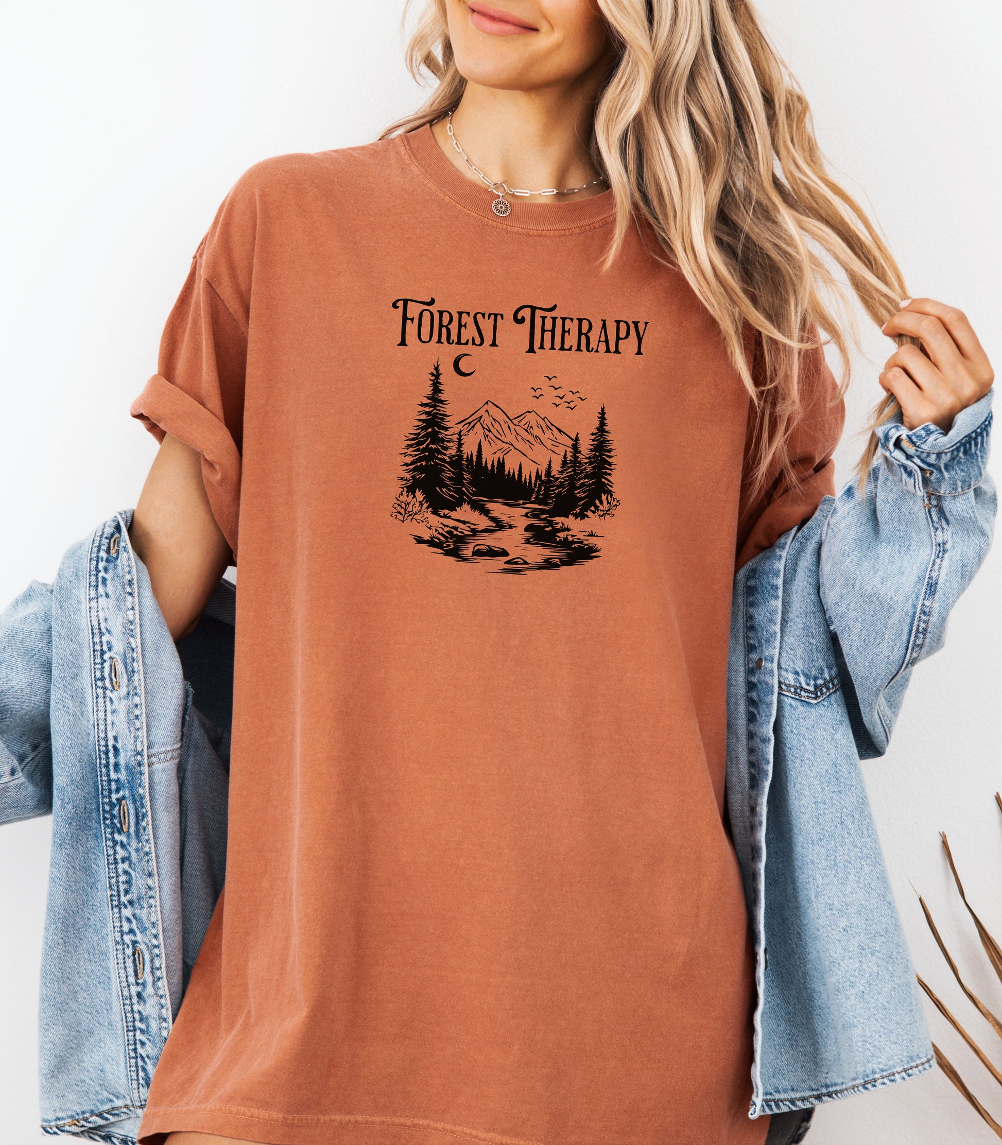 Person wearing a yam t-shirt featuring a black “Forest Therapy” design with a peaceful mountain scene, pine trees, a flowing river, birds, and a crescent moon. The perfect tee for nature lovers, hikers, and outdoor enthusiasts seeking serenity and scenic vibes.