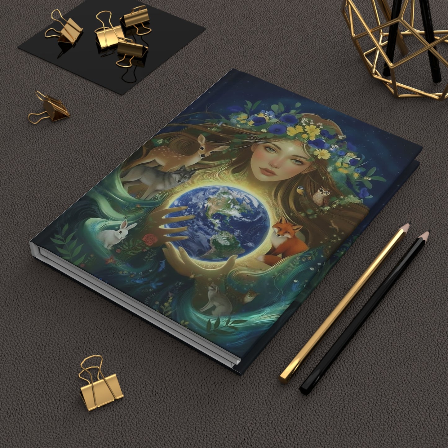 Gaia Earth Goddess Hardcover Journal with a colorful illustration of a woman holding the earth, surrounded by nature elements and woodland animals on a dark surface.