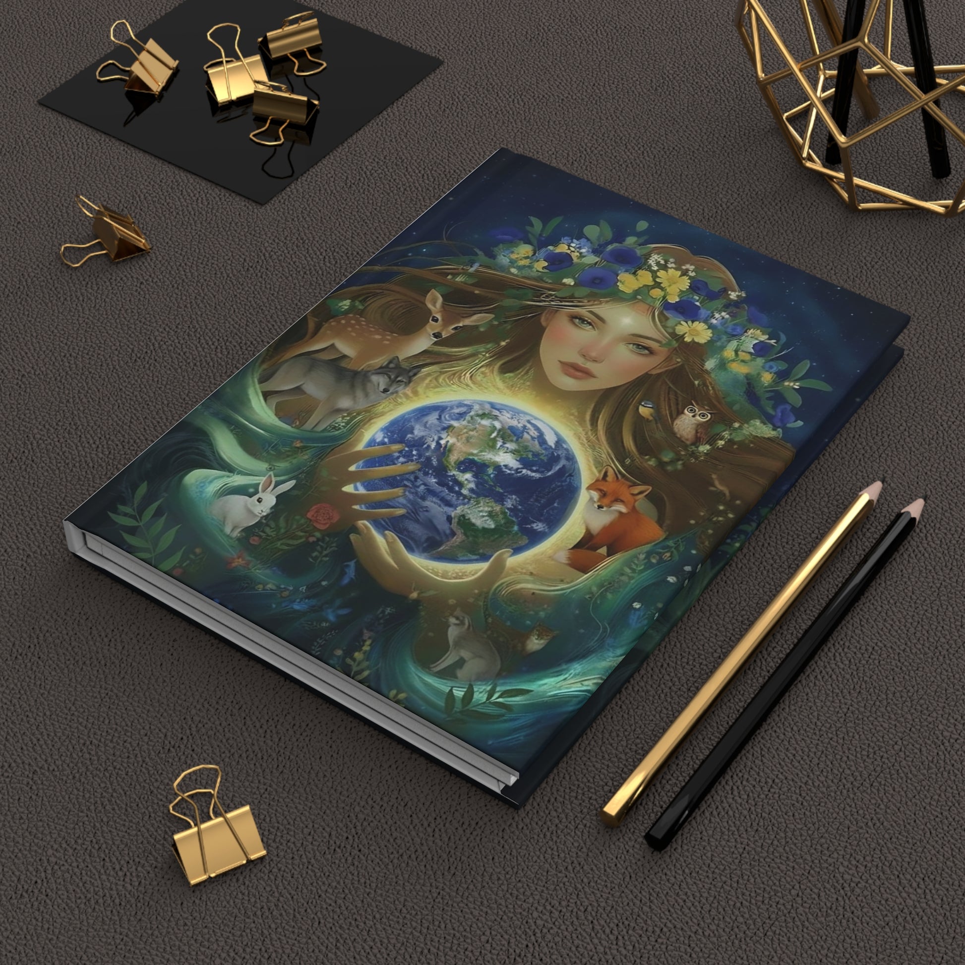 Gaia Earth Goddess Hardcover Journal with a colorful illustration of a woman holding the earth, surrounded by nature elements and woodland animals on a dark surface.