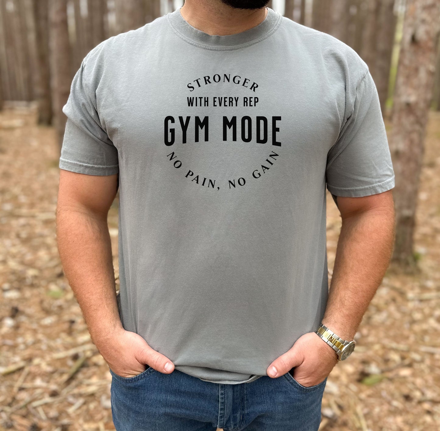 A person wearing a grey T-shirt with the bold black text “Stronger With Every Rep – Gym Mode – No Pain, No Gain.” The fitness-themed design features a curved text layout, perfect for workout enthusiasts and gym-goers who embrace strength training and motivation.