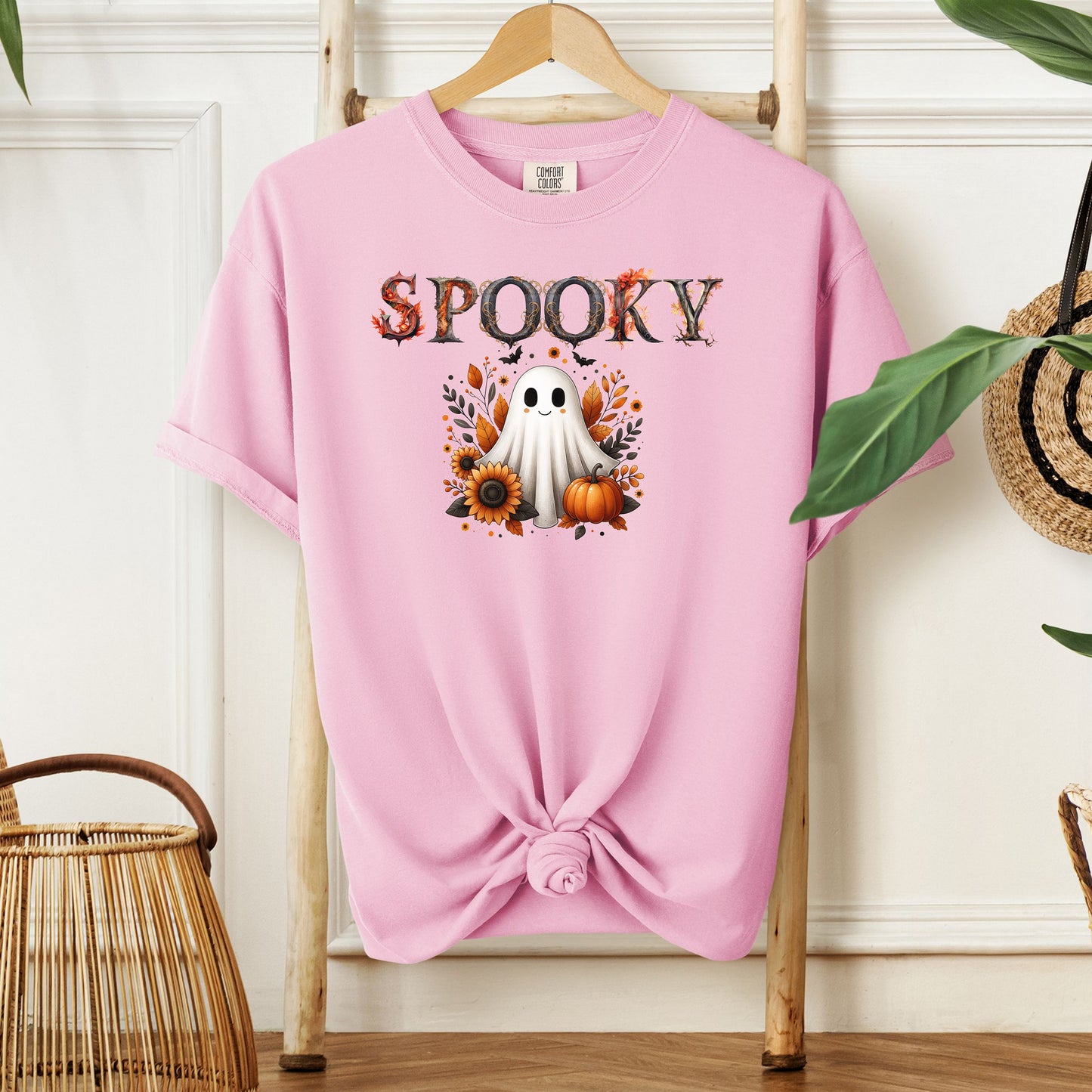Blossom pink T-shirt featuring a cute "Spooky" Halloween design with a smiling ghost surrounded by pumpkins, sunflowers, and autumn leaves. The word "Spooky" is styled with rustic wood-textured letters accented with fall foliage. Perfect for festive fall outfits, Halloween parties, or cozy seasonal wear.