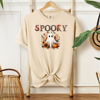 Ivory T-shirt featuring a cute "Spooky" Halloween design with a smiling ghost surrounded by pumpkins, sunflowers, and autumn leaves. The word "Spooky" is styled with rustic wood-textured letters accented with fall foliage. Perfect for festive fall outfits, Halloween parties, or cozy seasonal wear.