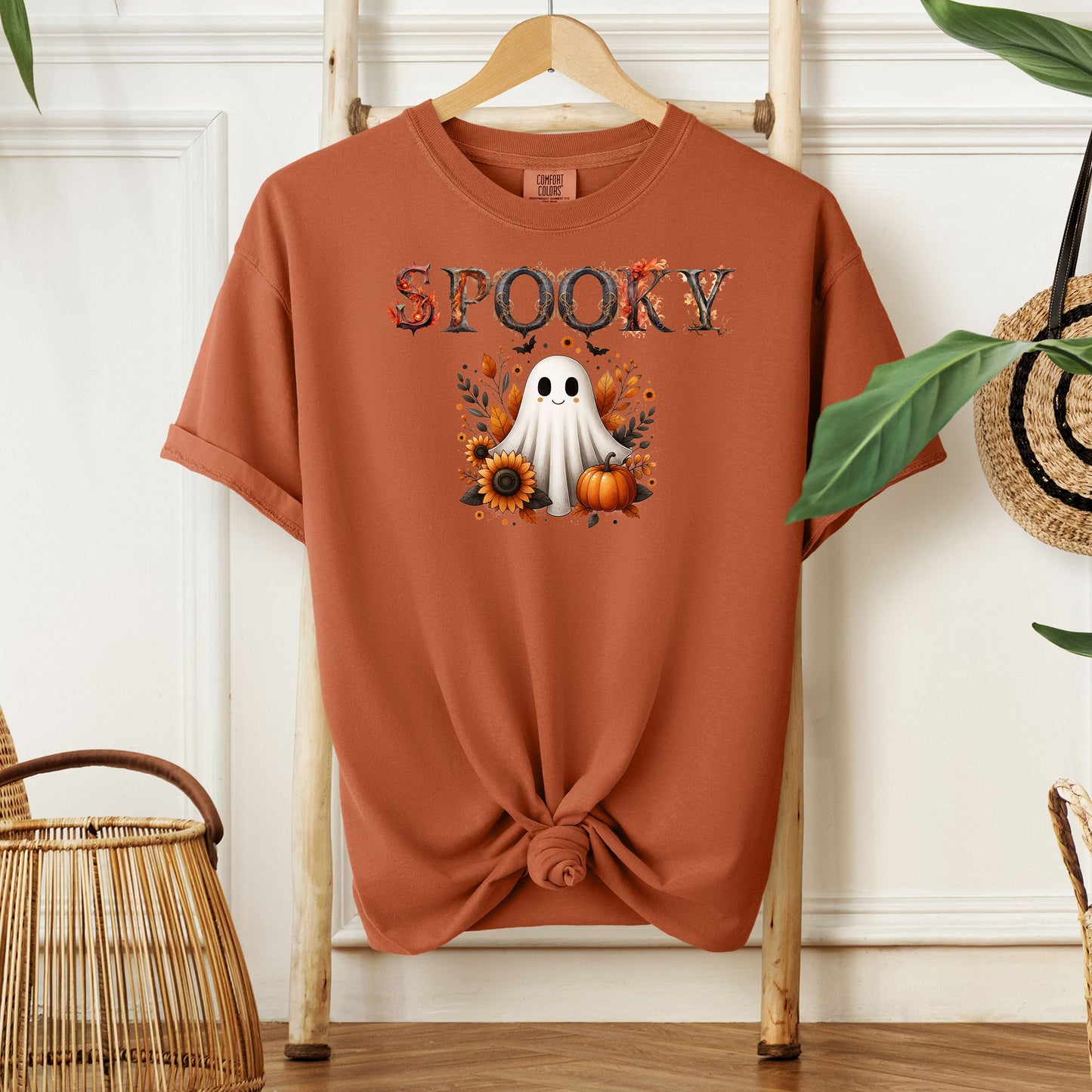 Yam T-shirt featuring a cute "Spooky" Halloween design with a smiling ghost surrounded by pumpkins, sunflowers, and autumn leaves. The word "Spooky" is styled with rustic wood-textured letters accented with fall foliage. Perfect for festive fall outfits, Halloween parties, or cozy seasonal wear.