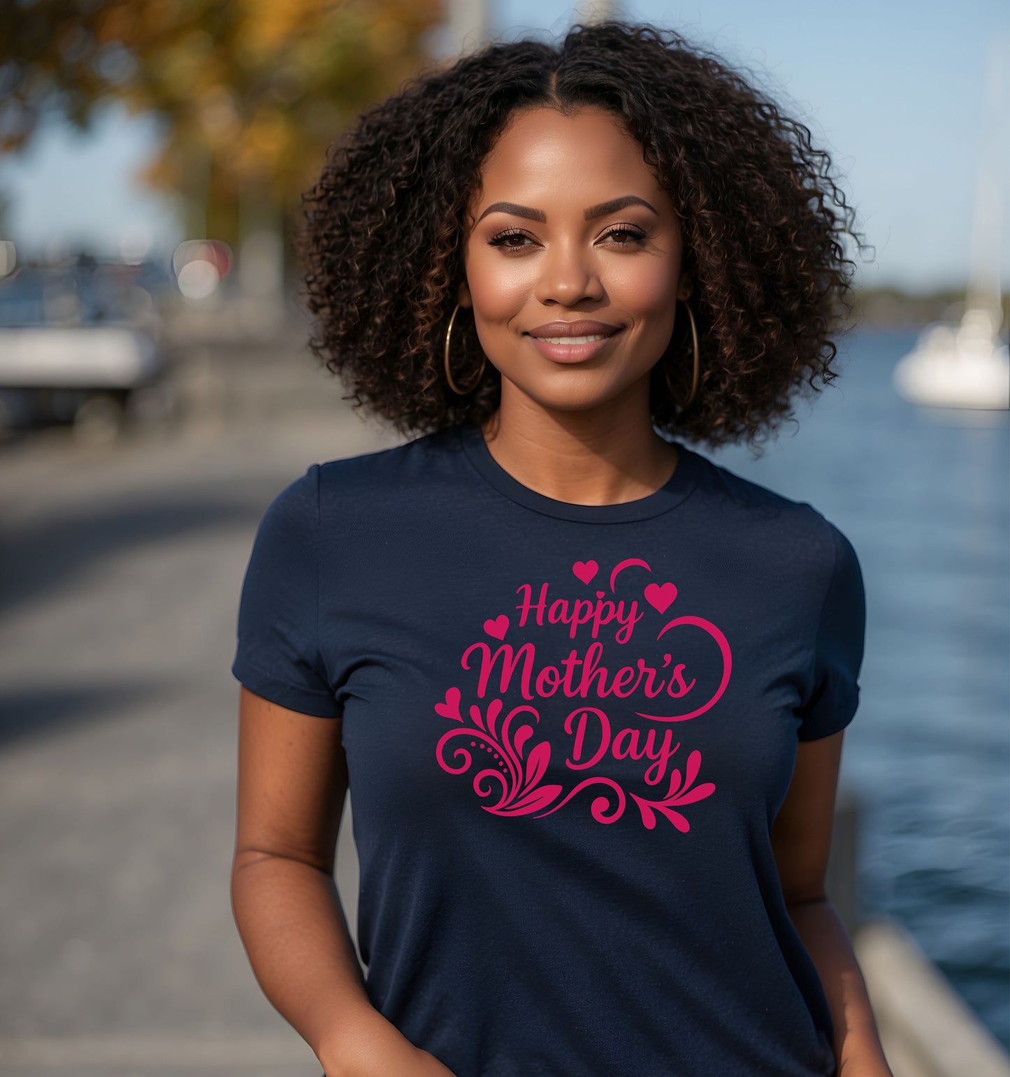 Woman wearing a navy blue t-shirt with 'Happy Mother's Day' in pink text, standing by a waterfront.
