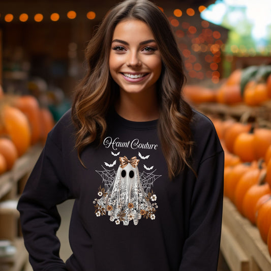 Black Gildan sweatshirt featuring a stylish “Haunt Couture” design with a chic ghost draped in lace, wearing a metallic bow, surrounded by floral accents, spiderwebs, and flying bats. A glamorous and spooky Halloween look that blends fashion and festive charm—perfect for fall outings and haunted style.