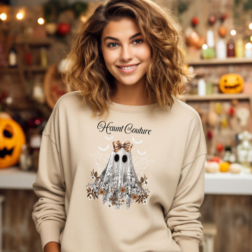 Sand Gildan sweatshirt featuring a stylish “Haunt Couture” design with a chic ghost draped in lace, wearing a metallic bow, surrounded by floral accents, spiderwebs, and flying bats. A glamorous and spooky Halloween look that blends fashion and festive charm—perfect for fall outings and haunted style.