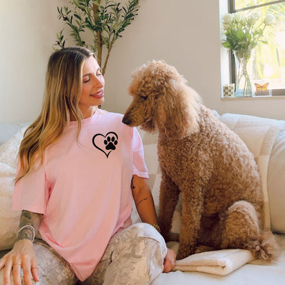 Person wearing a classic blossom pink T-shirt featuring a simple black heart outline with a paw print inside on the upper left chest. The minimalist Heart Paw Print design symbolizes love for pets, making it a perfect shirt for dog and cat lovers.