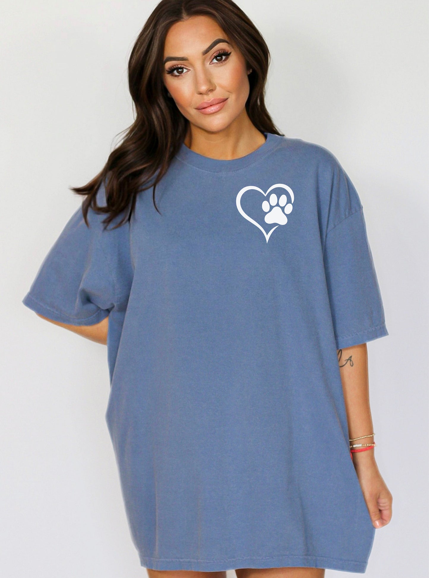 Person wearing a classic blue jean T-shirt featuring a simple white heart outline with a paw print inside on the upper left chest. The minimalist Heart Paw Print design symbolizes love for pets, making it a perfect shirt for dog and cat lovers.