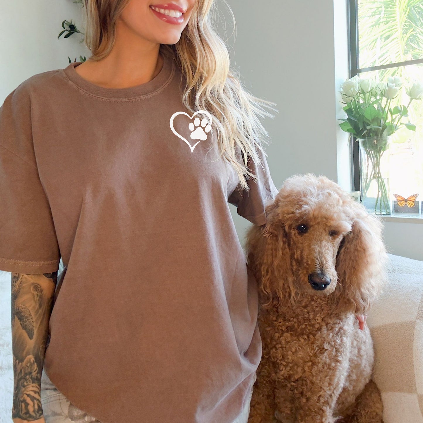 Person wearing a classic espresso T-shirt featuring a simple white heart outline with a paw print inside on the upper left chest. The minimalist Heart Paw Print design symbolizes love for pets, making it a perfect shirt for dog and cat lovers.
