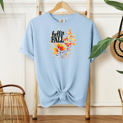 Chambray light blue T-shirt featuring a vibrant "Hello Fall" design with hand-painted autumn leaves in orange, yellow, and soft grey blue tones. The bold black lettering is accented by delicate foliage, giving this seasonal tee a cozy, cheerful, and nature-inspired look perfect for fall fashion.