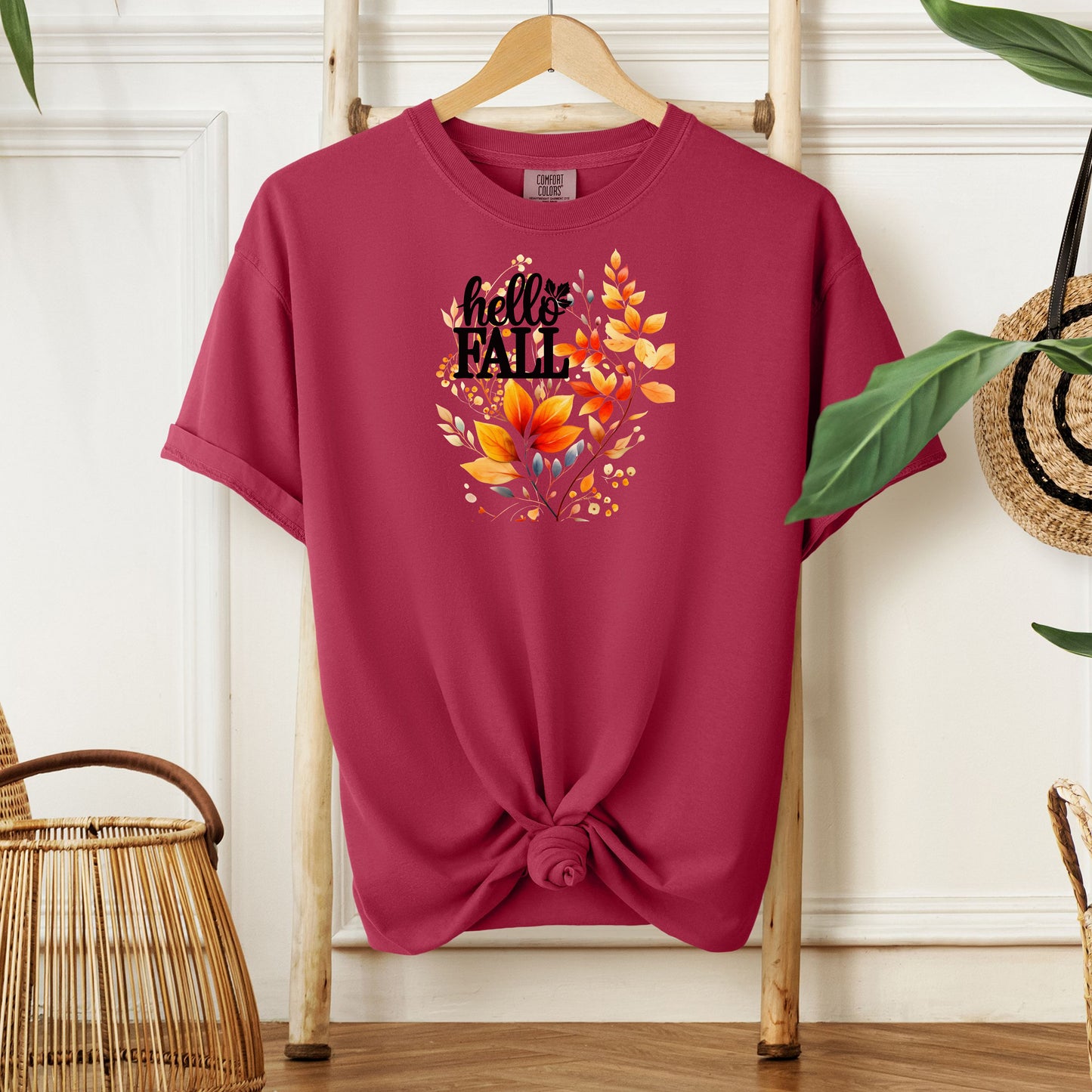 Chili T-shirt featuring a vibrant "Hello Fall" design with hand-painted autumn leaves in orange, yellow, and soft grey blue tones. The bold black lettering is accented by delicate foliage, giving this seasonal tee a cozy, cheerful, and nature-inspired look perfect for fall fashion.