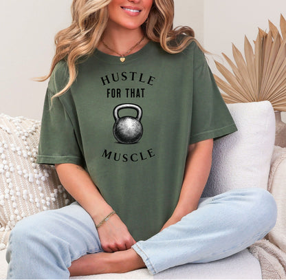 Person wearing a hemp color T-shirt with the phrase “Hustle For That Muscle” in bold black text, arched above and below a detailed kettlebell graphic. The design blends minimalist style with fitness motivation, perfect for gym-goers, weightlifters, and strength training enthusiasts who embrace hard work and dedication in their workout journey.