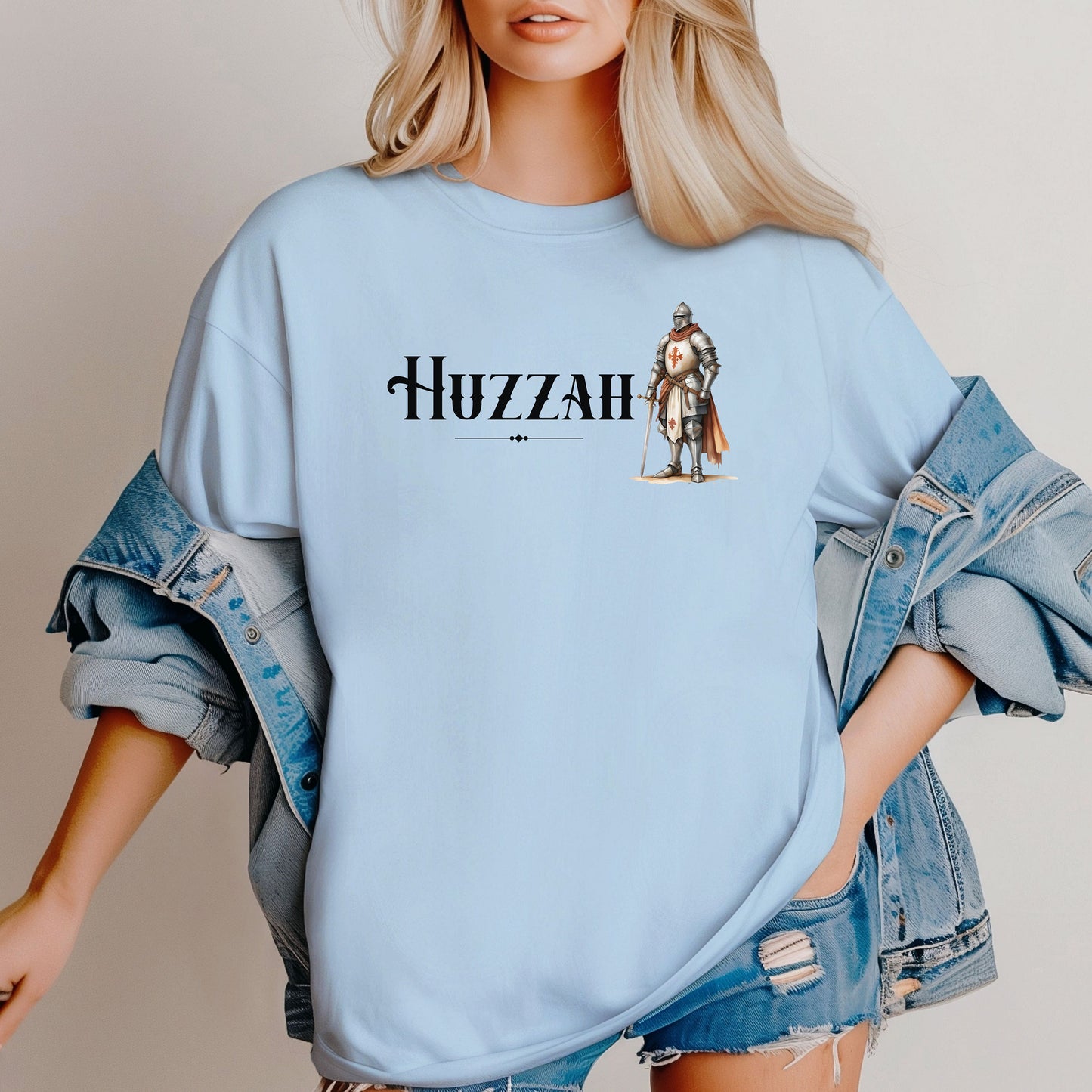 Chambray light blue T-shirt featuring a Renaissance Faire design with the word “Huzzah” in medieval-style lettering and an illustration of a knight in shining armor. Perfect for Renaissance fair goers, medieval enthusiasts, and fans of historical festivals, celebrating the lively and spirited call of “Huzzah” at fairs and events.
