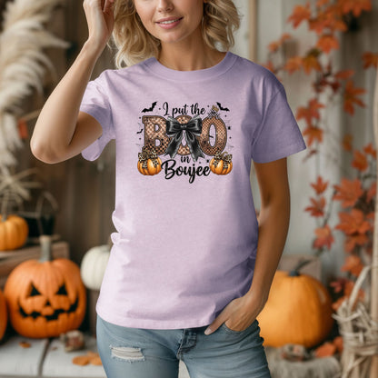Person wearing a Orchid t-shirt with the phrase "I put the BOO in Boujee" in bold, Halloween-themed lettering. The design features a black bow, leopard print accents, bats, sparkling stars, and orange pumpkins, combining spooky and glamorous elements. Perfect for stylish Halloween lovers with a boujee flair.