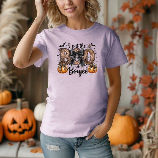 Person wearing a Orchid t-shirt with the phrase "I put the BOO in Boujee" in bold, Halloween-themed lettering. The design features a black bow, leopard print accents, bats, sparkling stars, and orange pumpkins, combining spooky and glamorous elements. Perfect for stylish Halloween lovers with a boujee flair.
