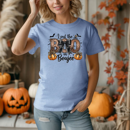 Person wearing a Washed Denim t-shirt with the phrase "I put the BOO in Boujee" in bold, Halloween-themed lettering. The design features a black bow, leopard print accents, bats, sparkling stars, and orange pumpkins, combining spooky and glamorous elements. Perfect for stylish Halloween lovers with a boujee flair.