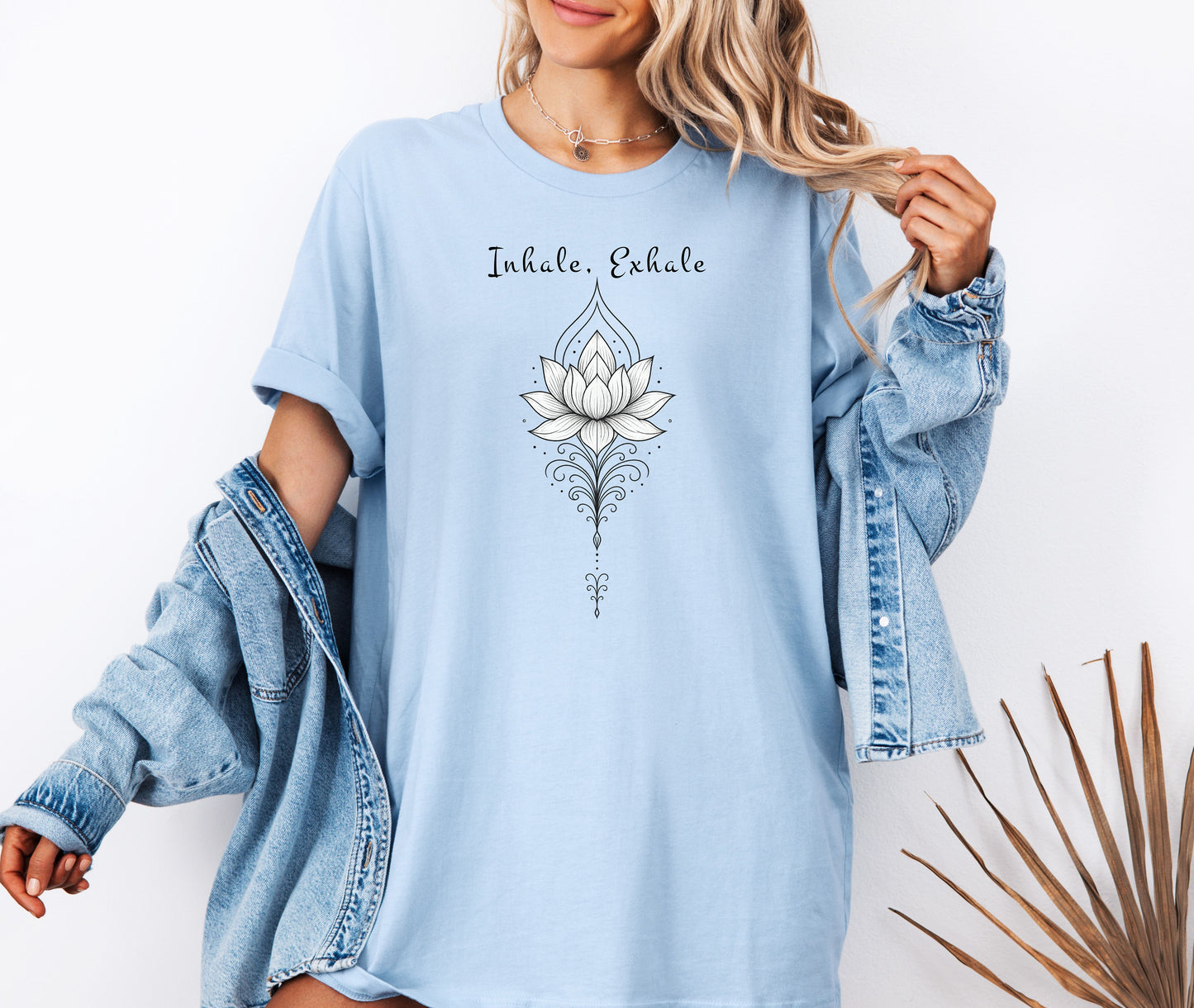 Person wearing a baby blue T-shirt featuring an elegant black line art lotus flower design with decorative flourishes, topped by the words “Inhale, Exhale” in a graceful script font. The minimalist, zen-inspired artwork conveys peace, mindfulness, and calm, making it perfect for yoga lovers, meditation enthusiasts, and those who embrace a serene, balanced lifestyle.
