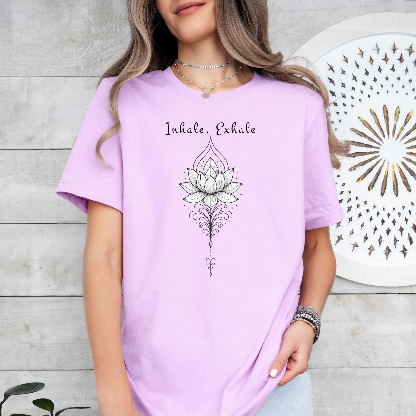 Person wearing a lilac T-shirt featuring an elegant black line art lotus flower design with decorative flourishes, topped by the words “Inhale, Exhale” in a graceful script font. The minimalist, zen-inspired artwork conveys peace, mindfulness, and calm, making it perfect for yoga lovers, meditation enthusiasts, and those who embrace a serene, balanced lifestyle.