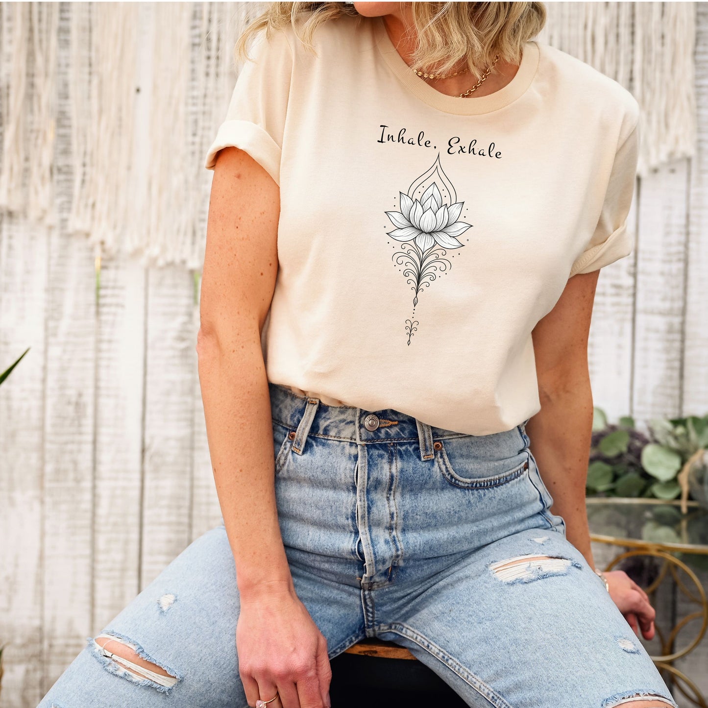 Person wearing a soft cream T-shirt featuring an elegant black line art lotus flower design with decorative flourishes, topped by the words “Inhale, Exhale” in a graceful script font. The minimalist, zen-inspired artwork conveys peace, mindfulness, and calm, making it perfect for yoga lovers, meditation enthusiasts, and those who embrace a serene, balanced lifestyle.