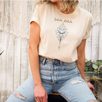 Person wearing a soft cream T-shirt featuring an elegant black line art lotus flower design with decorative flourishes, topped by the words “Inhale, Exhale” in a graceful script font. The minimalist, zen-inspired artwork conveys peace, mindfulness, and calm, making it perfect for yoga lovers, meditation enthusiasts, and those who embrace a serene, balanced lifestyle.
