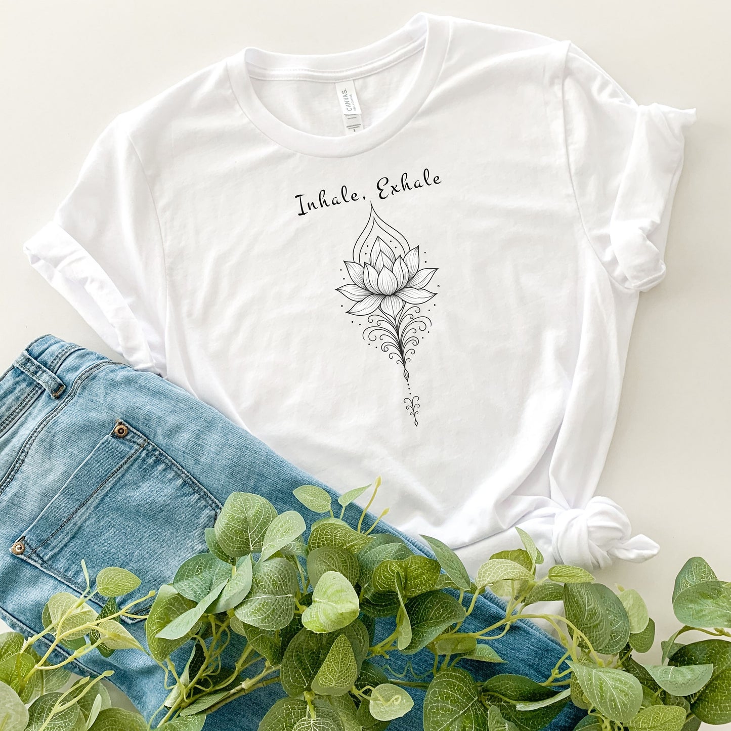 Person wearing a classic white T-shirt featuring an elegant black line art lotus flower design with decorative flourishes, topped by the words “Inhale, Exhale” in a graceful script font. The minimalist, zen-inspired artwork conveys peace, mindfulness, and calm, making it perfect for yoga lovers, meditation enthusiasts, and those who embrace a serene, balanced lifestyle.