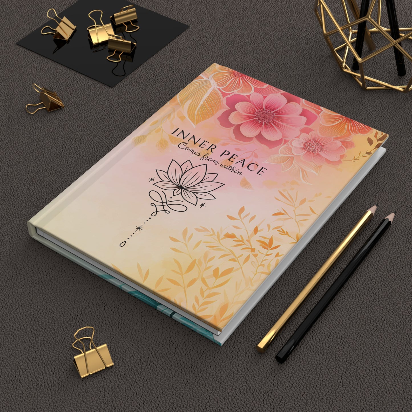 Hardcover journal with floral design and 'Inner Peace' text on a dark surface with stationery items.