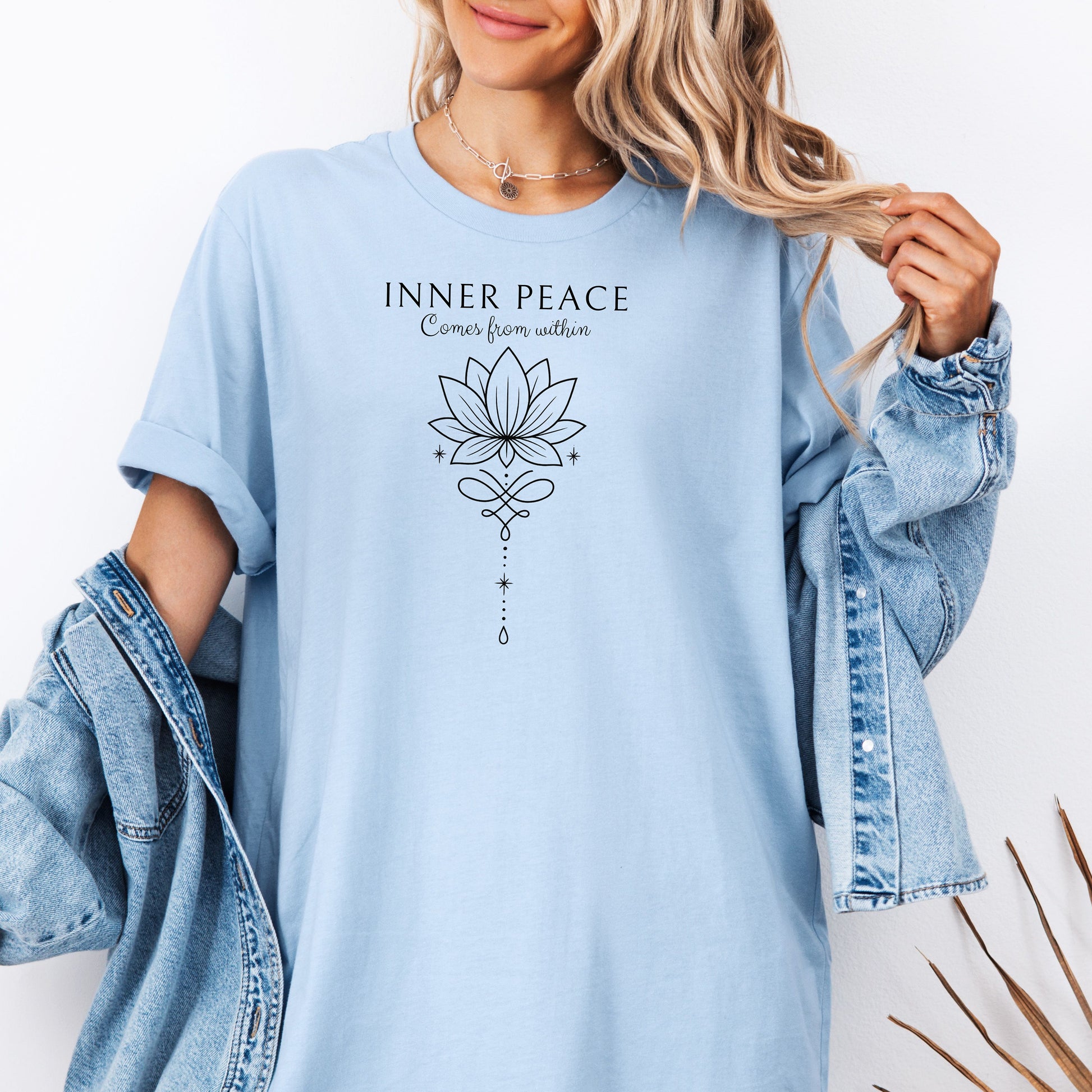 Person wearing a Chambray light blue T-shirt featuring an “Inner Peace Comes from Within” design with a black line art lotus flower and elegant ornamental accents. The minimalist, symmetrical artwork conveys tranquility, mindfulness, and spiritual balance, making it perfect for yoga enthusiasts, meditation lovers, and those seeking calm, positive energy in their everyday style.