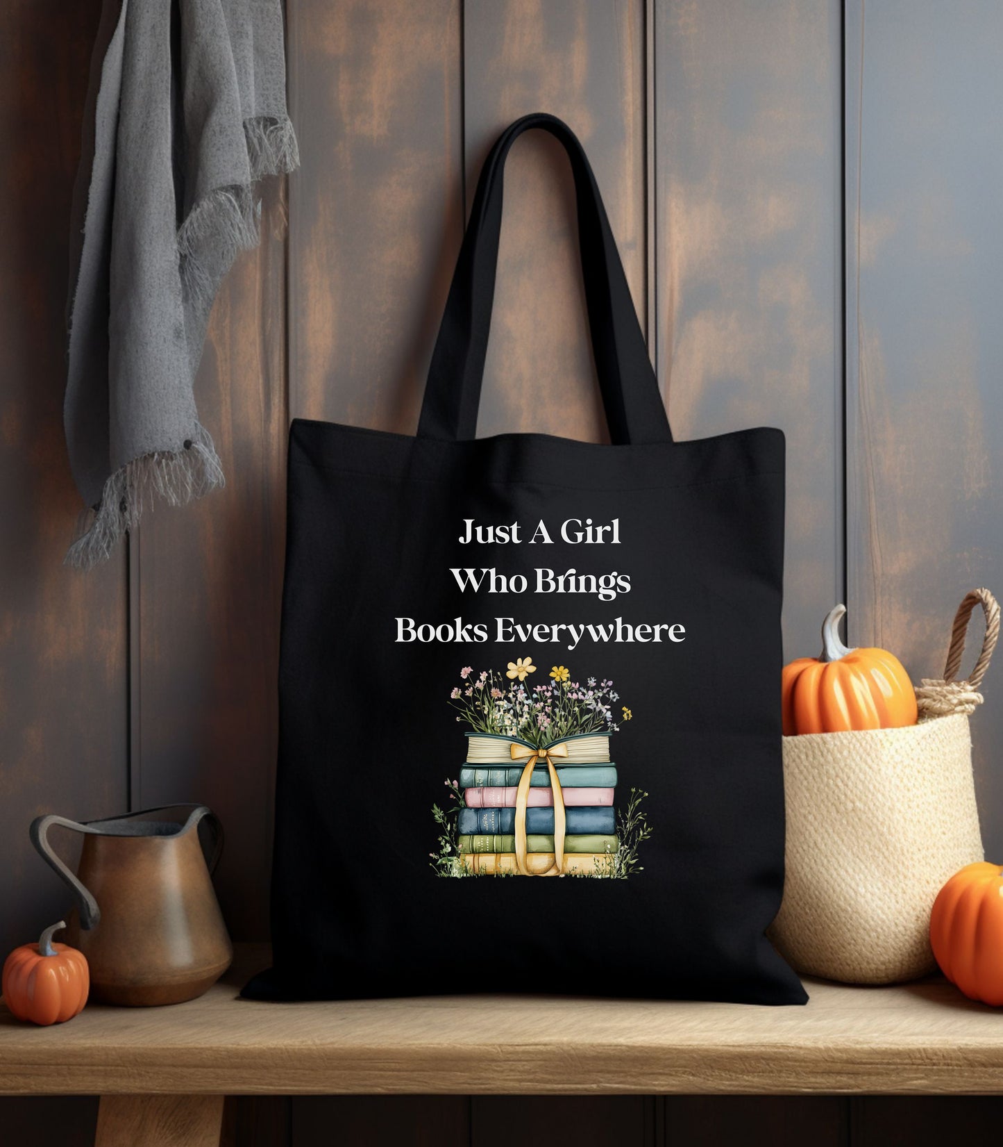 Black tote bag with 'Just A Girl Who Brings Books Everywhere' text and book illustration, surrounded by flowers.