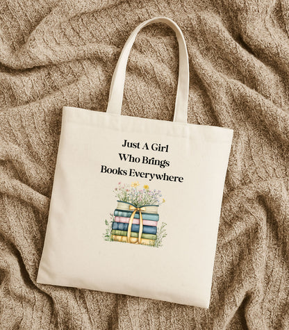 Natural tote bag with 'Just A Girl Who Brings Books Everywhere' text and book illustration, surrounded by flowers.