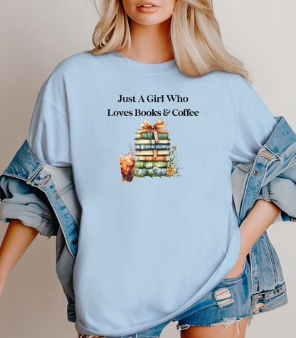 Woman wearing a Chambray light blue t-shirt with the phrase "Just A Girl Who Loves Books & Coffee" printed above a charming stack of pastel-colored books tied with a ribbon, surrounded by fall foliage and a glass of iced coffee. A cozy and whimsical design perfect for bookworms and coffee lovers alike.