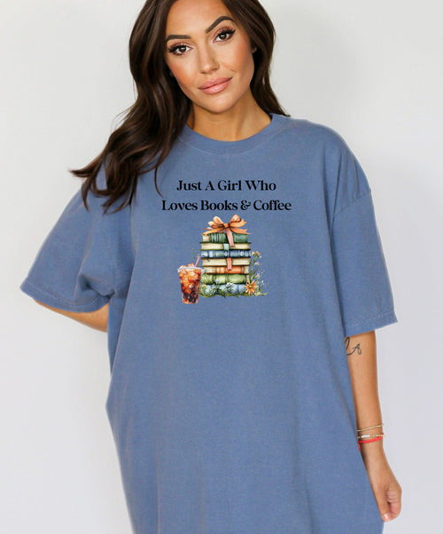 Woman wearing a Washed Denim t-shirt with the phrase "Just A Girl Who Loves Books & Coffee" printed above a charming stack of pastel-colored books tied with a ribbon, surrounded by fall foliage and a glass of iced coffee. A cozy and whimsical design perfect for bookworms and coffee lovers alike.