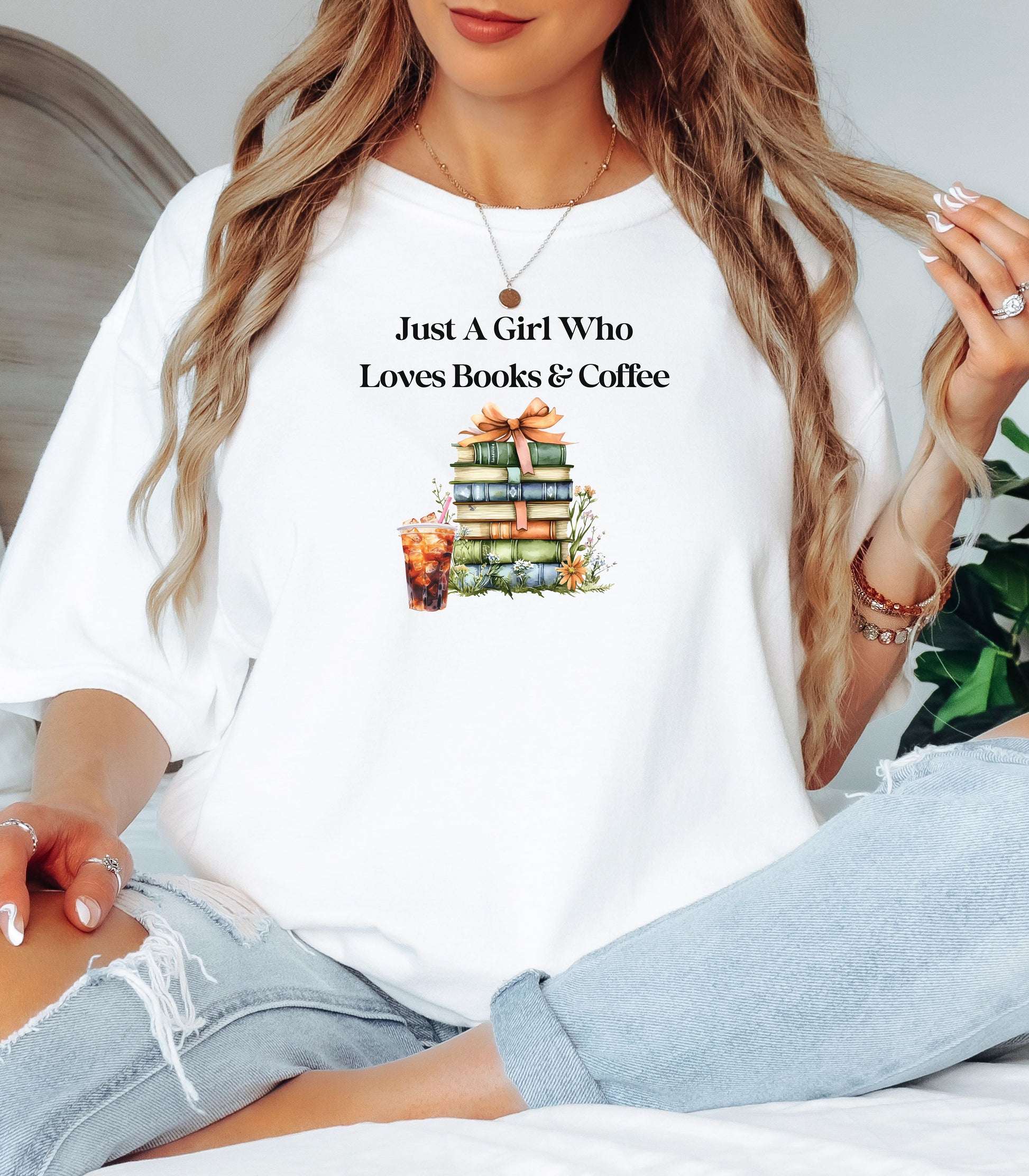 Woman wearing a White t-shirt with the phrase "Just A Girl Who Loves Books & Coffee" printed above a charming stack of pastel-colored books tied with a ribbon, surrounded by fall foliage and a glass of iced coffee. A cozy and whimsical design perfect for bookworms and coffee lovers alike.