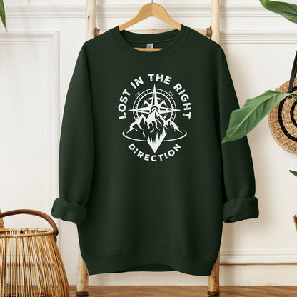 Forest sweatshirt featuring a white graphic design of a mountain range with a compass rising behind it, surrounded by pine trees. The words "Lost In The Right Direction" curve around the design, blending adventure and wanderlust vibes. Perfect for outdoor enthusiasts, hikers, and travelers seeking inspiration and style in casual wear.