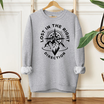 Sport Grey sweatshirt featuring a black graphic design of a mountain range with a compass rising behind it, surrounded by pine trees. The words "Lost In The Right Direction" curve around the design, blending adventure and wanderlust vibes. Perfect for outdoor enthusiasts, hikers, and travelers seeking inspiration and style in casual wear.