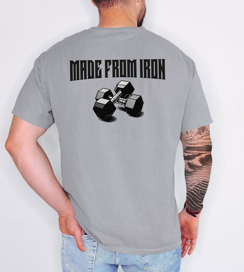 Person wearing a grey T-shirt with a bold back design that reads “Made From Iron” in strong, block lettering above an illustration of two black dumbbells. The graphic captures a powerful, fitness-inspired aesthetic, perfect for gym enthusiasts, weightlifters, and strength training fans who want to showcase their dedication and passion for lifting.