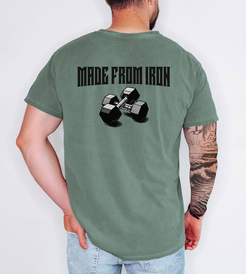 Person wearing a moss T-shirt with a bold back design that reads “Made From Iron” in strong, block lettering above an illustration of two black dumbbells. The graphic captures a powerful, fitness-inspired aesthetic, perfect for gym enthusiasts, weightlifters, and strength training fans who want to showcase their dedication and passion for lifting.
